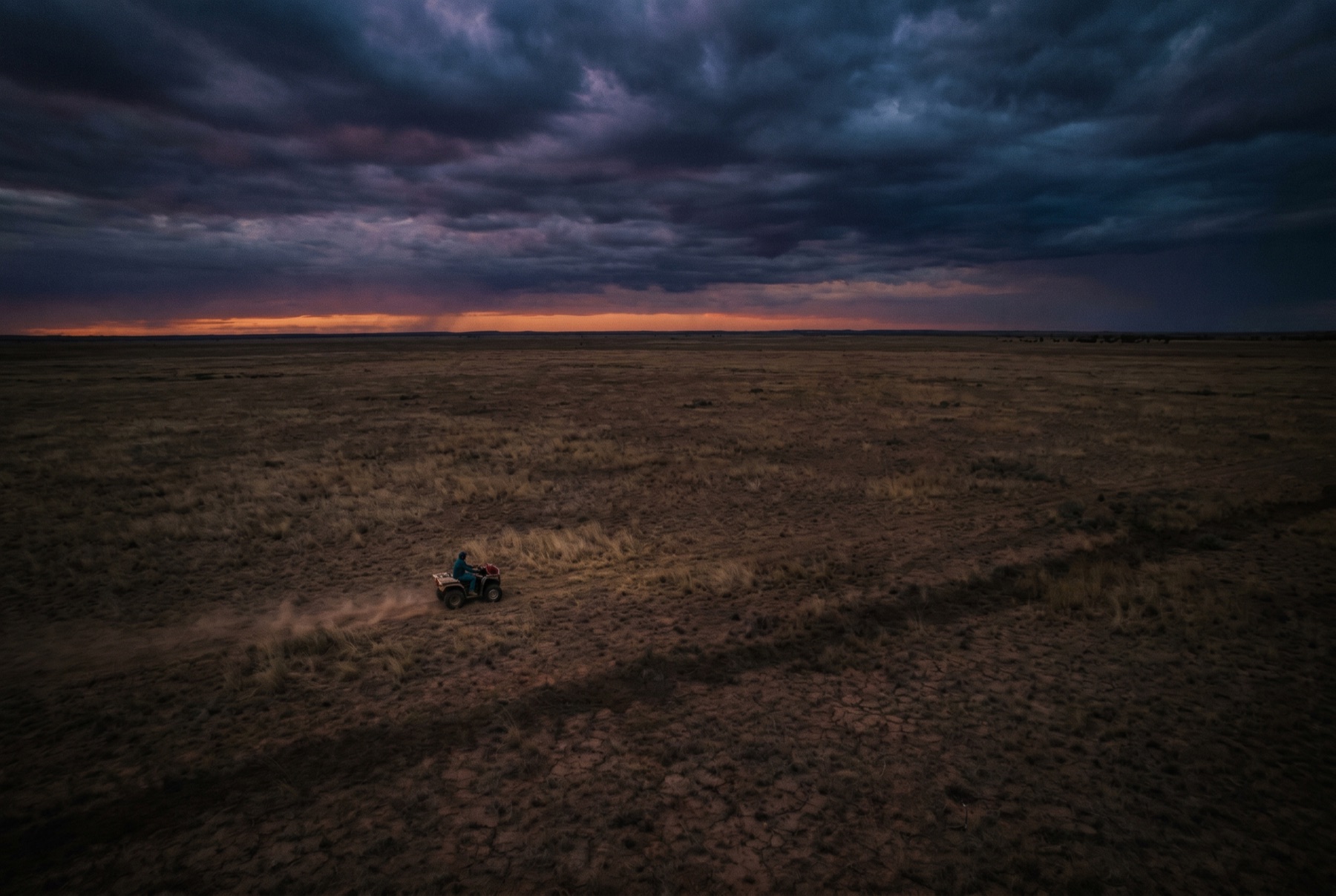 A lone farmer on a quad bike, small against an enormous paddock at dusk.